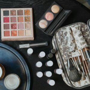 High-angle shot of cosmetics including brushes and an eyeshadow palette on a dark surface.