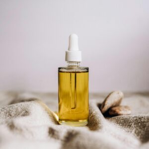 Close-up of a glass serum bottle with yellow liquid on woven fabric, showcasing elegance and simplicity.